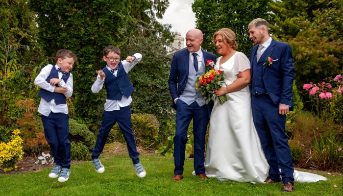A beautiful photo of a bride and groom on their wedding day at Lucan Spa Hotel alongside a groomsman and two children, who are jumping for joy in the air.